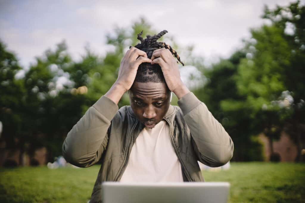 difficult writing ~ Upset young African American male freelancer clutching head with hands after failure in project while working remotely in park