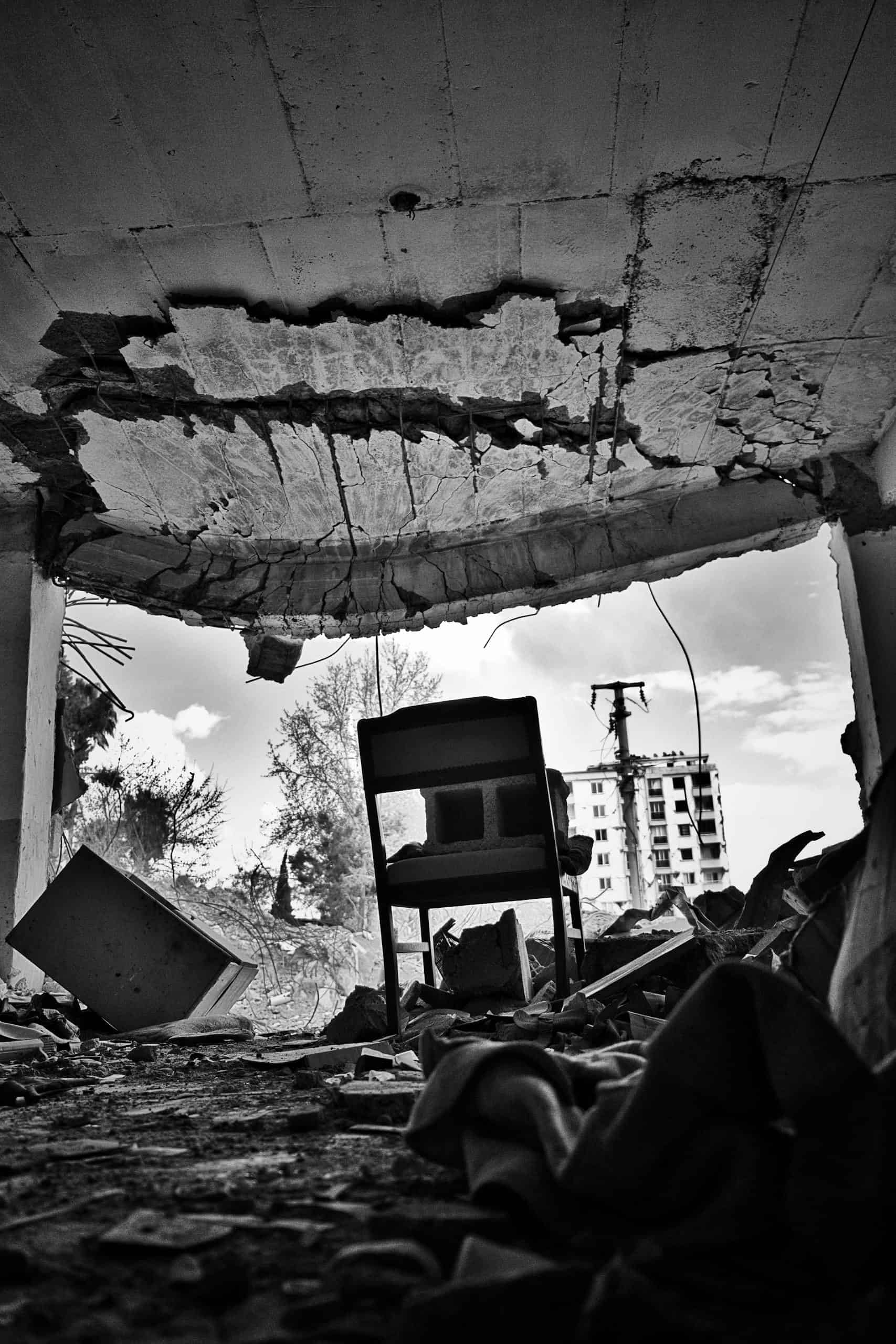 A black and white image of a ruined urban interior with collapsed ceiling and debris, showcasing disaster impact.