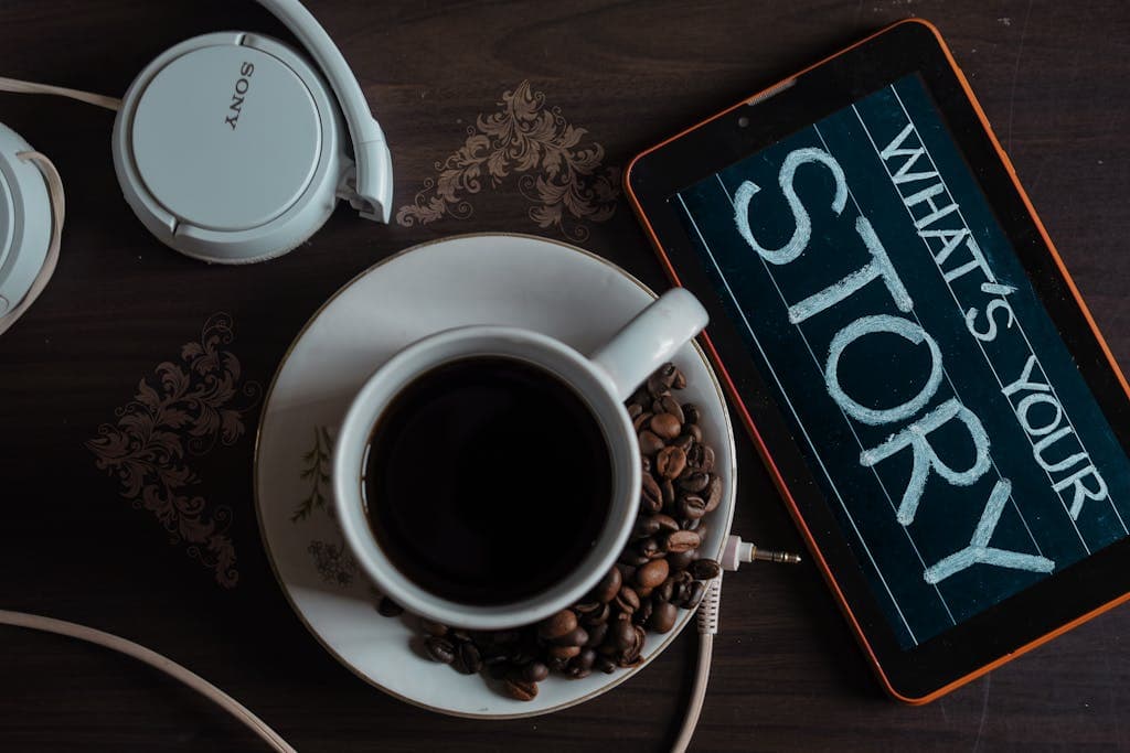 Weekly Writing Prompt ~ Flat lay of coffee cup, headphones, and tablet with 'What's Your Story' on screen.