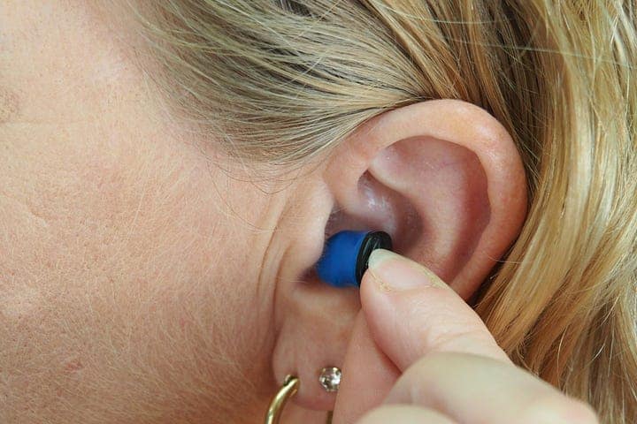 A woman placing a hearing device in her left ear